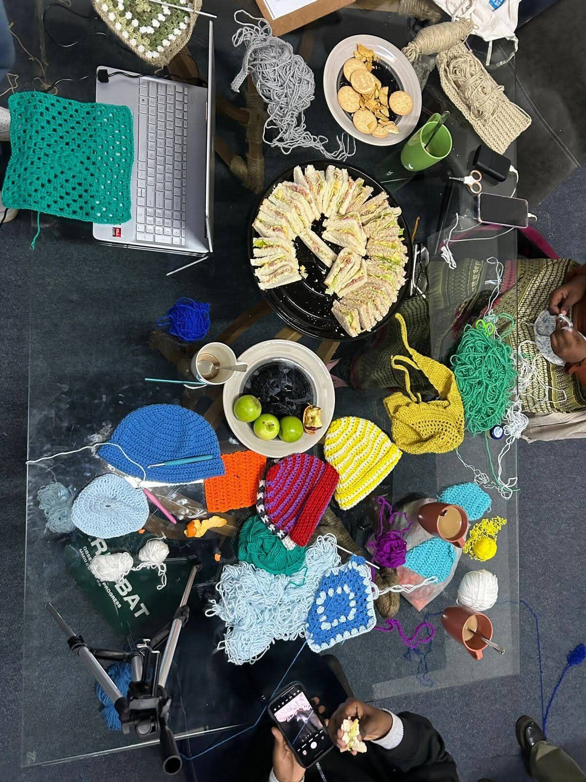 Overhead view of beanies in progress, tea, and sandwiches at a crochet meetup
